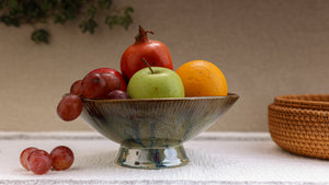 Fruit bowl with apples, oranges, and grapes on a neutral background