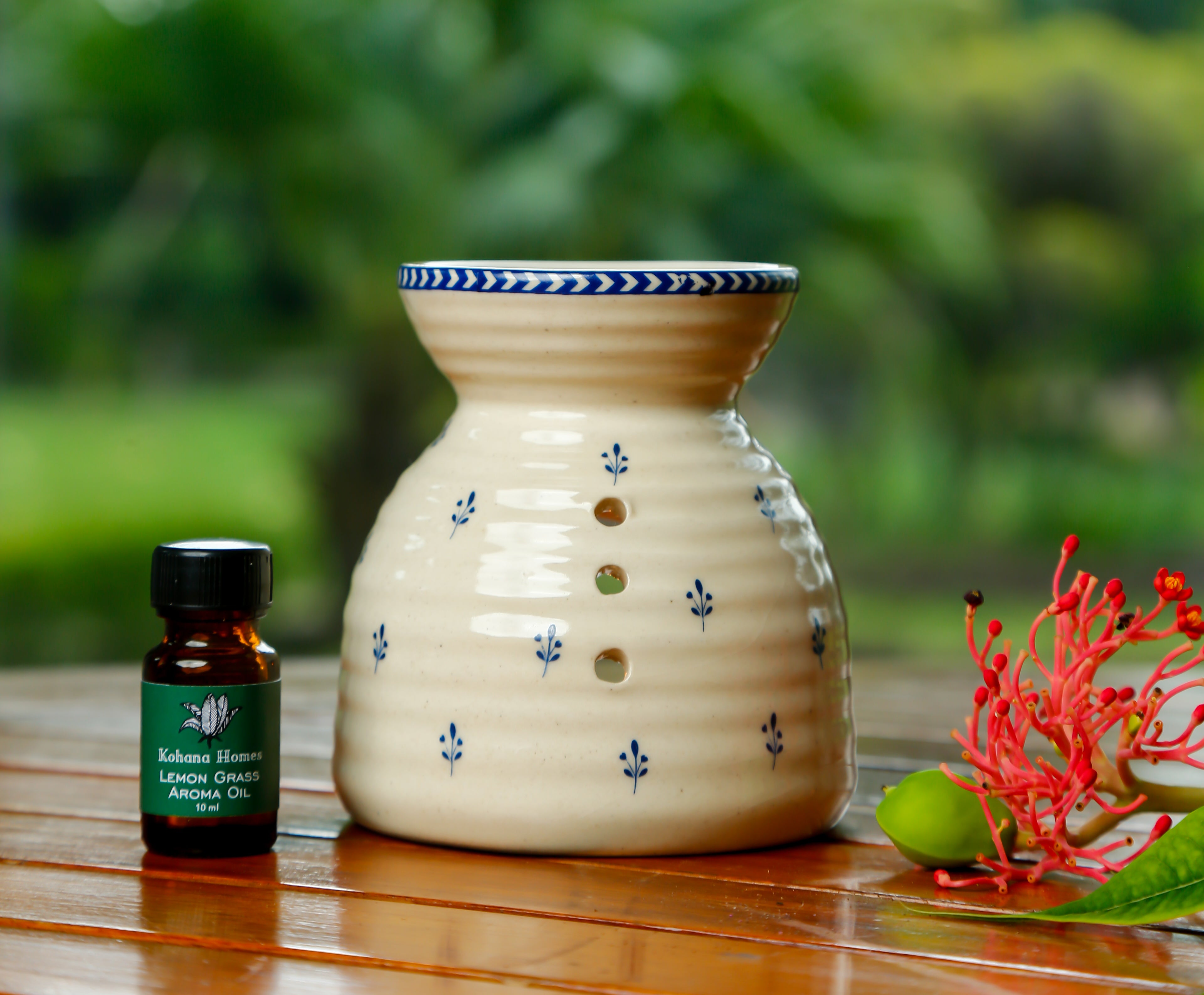 Ceramic diffuser with chintz print on a wooden surface, next to a bottle of essential oil and a red flower.
