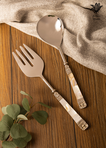 Decorative fork and spoon with shell handles on a wooden surface with a cloth and leaves.