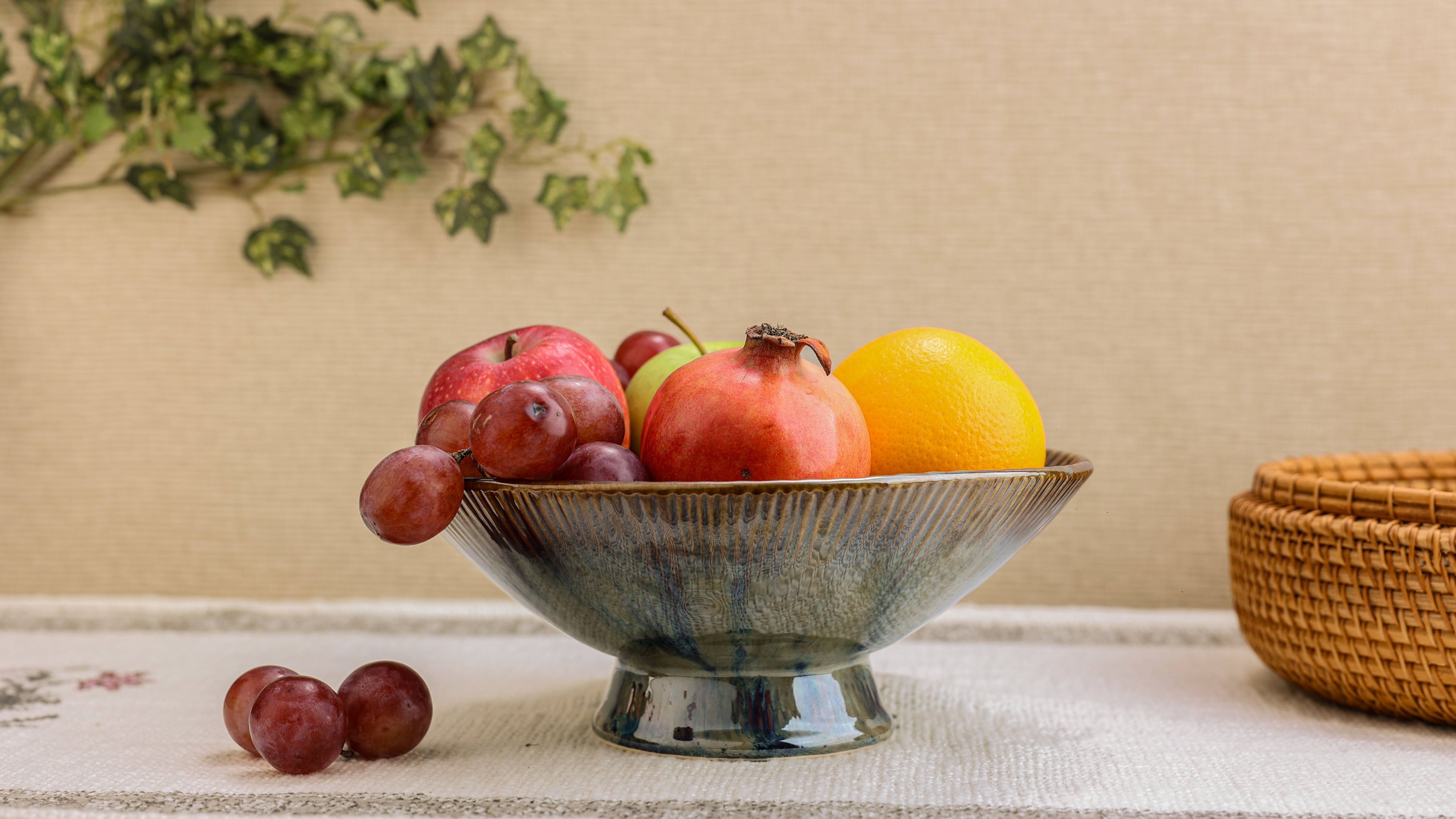 Fruit bowl with apples, pomegranate, and an orange on a textured surface with a woven basket in the background.
