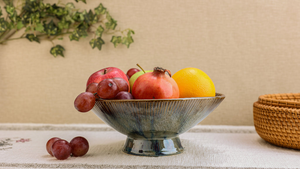 Fruit bowl with apples, pomegranate, and an orange on a textured surface with a woven basket in the background.