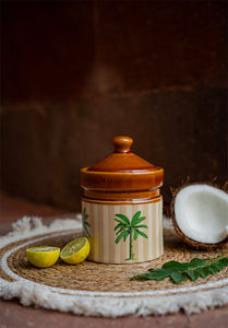 Ceramic jar with a lid on a woven mat with lemons and a coconut