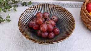 Red grapes in a decorative ceramic bowl on a light surface with greenery in the background